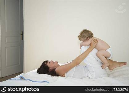 A mother laying down with legs bent holding a toddler on them