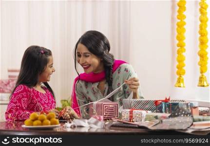 A mother packing gift with her daughter amidst presents,sweets,Diwali light and festive flower garland decoration.