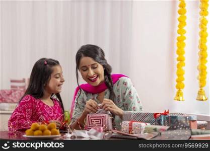 A mother packing gift with her daughter amidst presents,sweets,Diwali light and festive flower garland decoration.