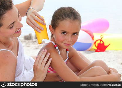 a mother putting sun cream on her daughter&acute;s shoulders