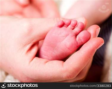 A mother&rsquo;s hand holding the foot of her baby