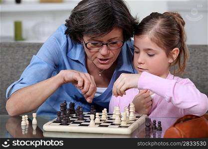 A mother teaching her daughter how to play chess.
