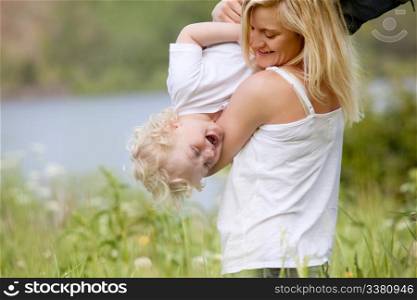 A mother tickling and playing with excited happy son in a green meadow