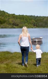 A mother walking with her son hear a lake with a small boat