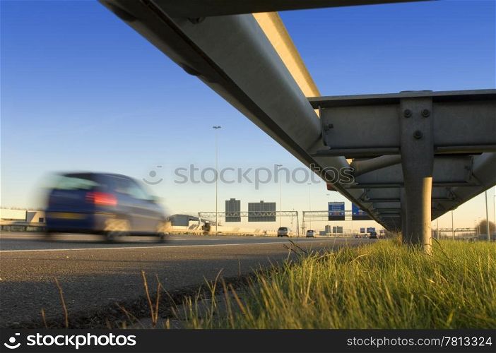 A motorway safety rail with route information sign and motion blurred passing cars