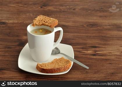 A mug of vegetable soup displayed with a broken pieces of whole wheat bread on a wooden background