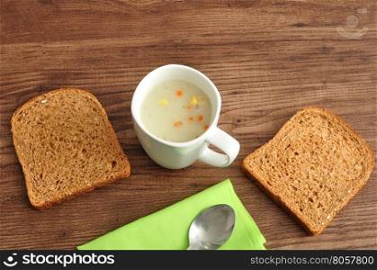 A mug of vegetable soup displayed with bread, a green napkin and a spoon on a wooden background