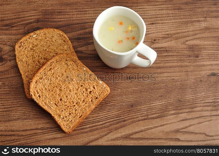 A mug of vegetable soup displayed with two slices of whole wheat bread on a wooden background