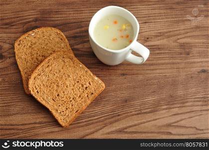 A mug of vegetable soup displayed with two slices of whole wheat bread on a wooden background