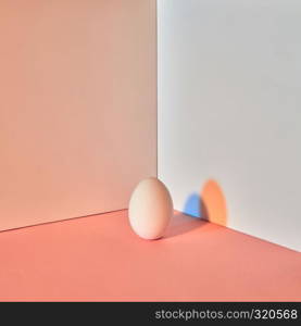 A multi-colored egg on a gray-beige double background with a reflection of blue-orange shadows and copy space for text. Easter layout. Colored egg with a reflection of blue-orange shadows around a double-beige-gray background with copy space. Easter concept.