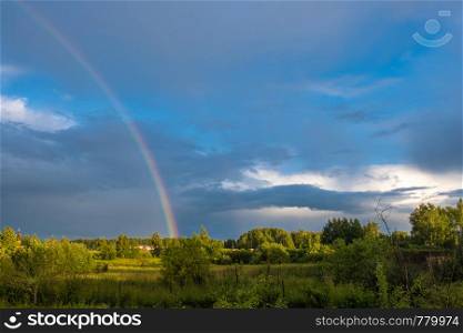 A multicolor rainbow against a dark cloudy sky on a summer day, Russia.