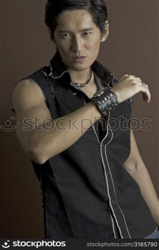 A muscular asian male model in a black waistcoat and a studded bracelet