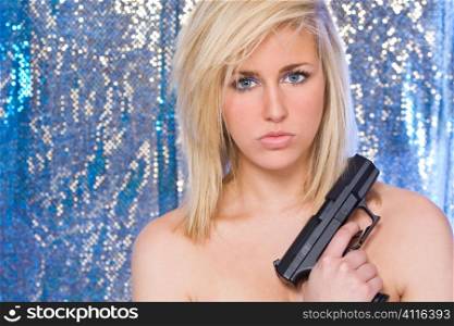 A naked beautiful blond haired blue eyed model holding a hand gun or pistol shot in a studio in front of a sparkling blue background.