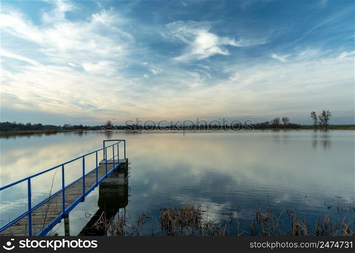 A narrow jetty on a calm lake and clouds, Staw, Poland