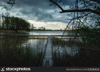 A narrow pier in the reeds of the lake and the cloudy sky, Stankow, Poland