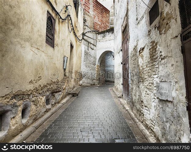 A narrow street in the old city of the Fez medina in Morocco leads up the hillside through an arch.