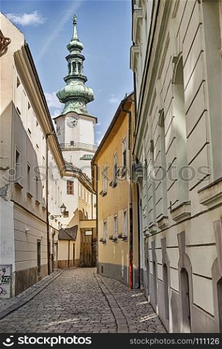 A narrow street of cobblestones leads towards the belltower of a church in the Old Town of Bratislava in Slovaka.