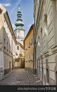 A narrow street of cobblestones leads towards the belltower of a church in the Old Town of Bratislava in Slovaka.