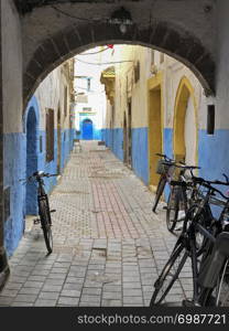 A narrow street, or alley, just off the main street is empty except for some bikes. This is in the souk of center of the old city of Essaouira, Morocco.