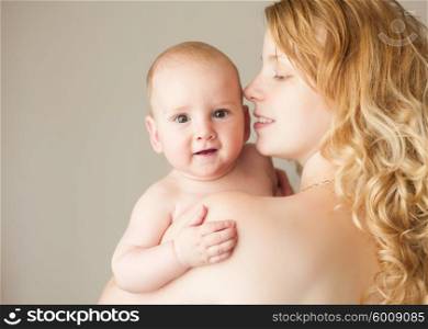 A natural blonde caucasian mother kissing happy baby. Mother and baby