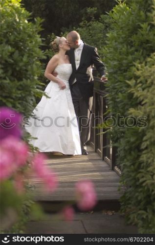 A newly married couple kissing on a wooden bridge
