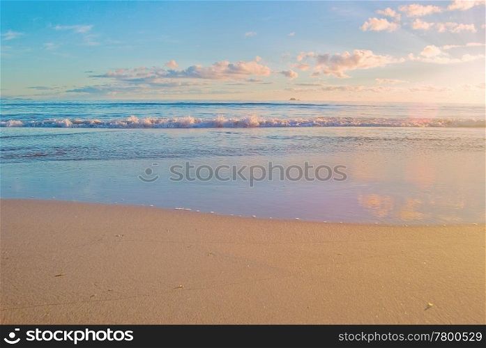 a nice beach scene with gentle waves reaching the sand at sunrise. beach sunrise scene