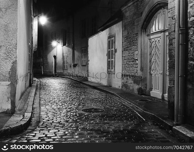 A night scene captures an empty alleyway in Beaune, France where the wet cobblestones are shining with lreflected ight from the street lights. (Scanned from black and white film.)