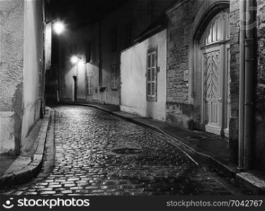 A night scene captures an empty alleyway in Beaune, France where the wet cobblestones are shining with lreflected ight from the street lights. (Scanned from black and white film.)