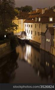 A night view of one of the canals in Prague as seen from the Charles Bridge. At the end, an old water wheel is slowly turning, creating a blur in the evening light.