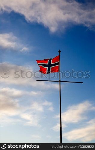 A norwegian flag blowing in the wind against a blue sky