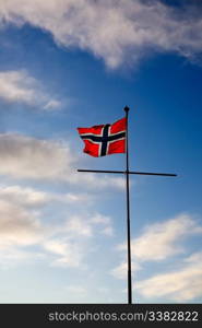 A norwegian flag blowing in the wind against a blue sky