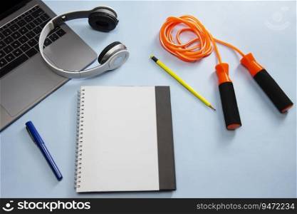 A notepad,skipping rope,pencil,pen,headphones and laptop kept together on plain surface.