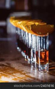 A number of shots with golden tequila and orange slices. Close-up