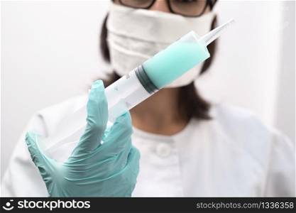 A nurse wearing a mask and gloves holding a syringe of virus vaccine in a modern clinic