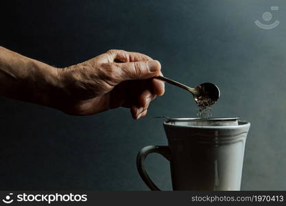 A old hand preparing a tea over a dark background with copy space and dark tones