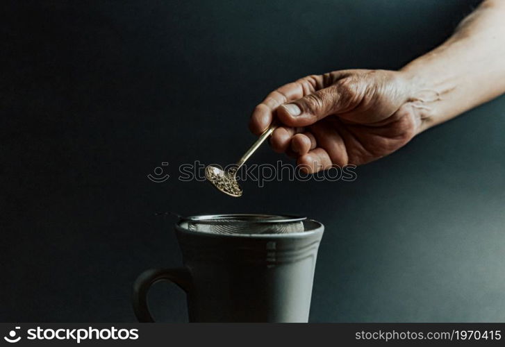 A old hand preparing a tea over a dark background with copy space and dark tones