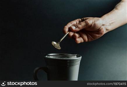 A old hand preparing a tea over a dark background with copy space and dark tones