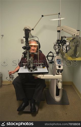 A older man sitting in the office of an optometrist checking out hiseyesight.