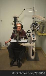 A older man sitting in the office of an optometrist checking out hiseyesight.