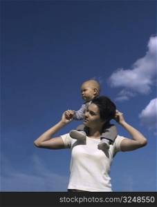 A one year old baby and his mom are spending some time together outdoor. The background is the clear blue sky.