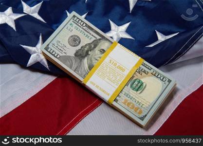 a pack with ten thousand dollars in hundred dollar bills lies against the backdrop of a starry striped American flag. us flag dollars