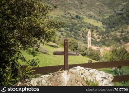 A painted wooden cross in the rock next to an olive tree and in front of the church tower at Moltifao in the Balagne region of Corsica