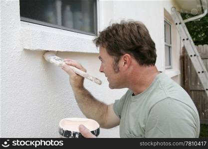 A painter edging around an exterior window with a brush.