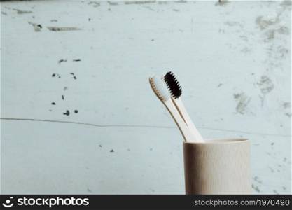 A pair of bamboo toothbrushes over a white wooden background inside a bamboo bottle with copy space
