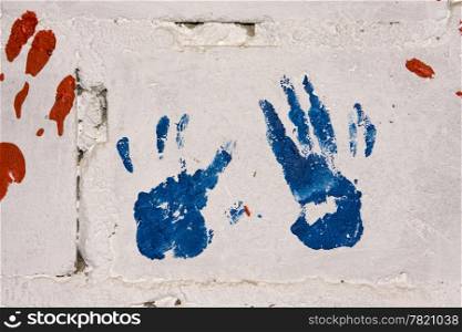 A pair of blue and red handprints on a white concrete wall make a colorful display on a preschool wall in a township in South Africa.