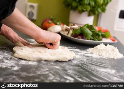 A pair of female hands are kneading bread dough into a pizza form.