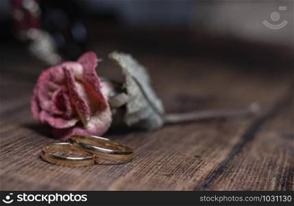 A pair of gold wedding rings on wooden background, in front of a flower.