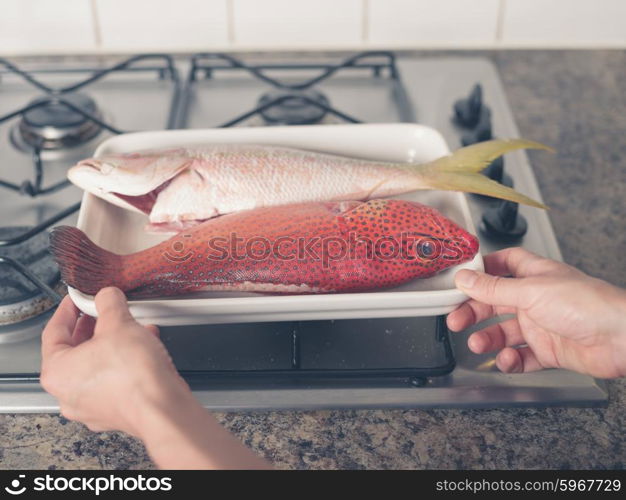 A pair of hands are placing a tray with two exotic fish on a stove
