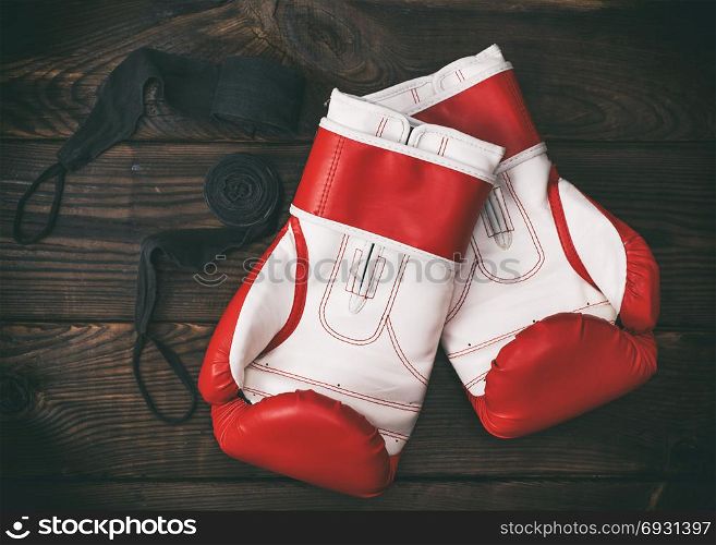 a pair of leather red boxing gloves and a black bandage on a brown wooden background