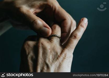 A pair of old hands grabbing a jewelry ring on the finger over a dark background
